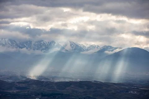 Sun light piercing through the clouds and hitting the mountains Stock Photos