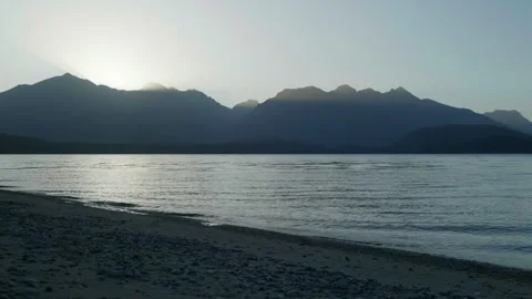 Sun light rays shining through mountain behind lake 스톡 동영상 260370021