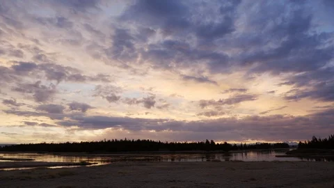 Sun lights up purple clouds over placid mountain river in Idaho Stock Footage 121016431