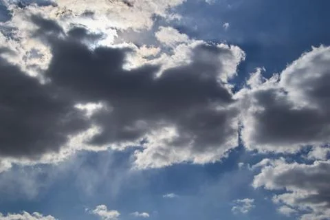 The sun makes the way through dark clouds in the blue sky. Stock Photos