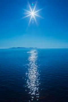 Sun over Mediterranean sea with small boat and landmass in the background. Stock Photos