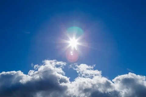 Sun over white cloud on blue sky background with natural lens flares Stock Photos
