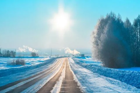 The sun over the winter forest highway and the settlement Krasnogorskiy at su Stock Photos