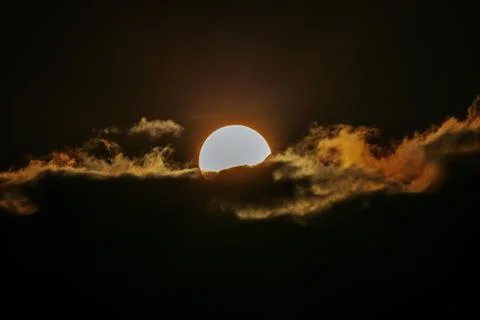 Sun partially obscured by dark clouds during sunset, with warm orange and y.. Stock Photos