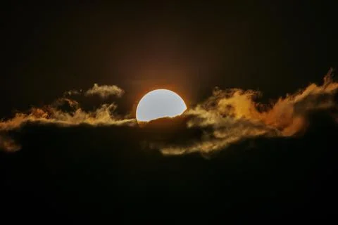 Sun partially obscured by dark clouds during sunset, with vibrant orange an.. Stock Photos