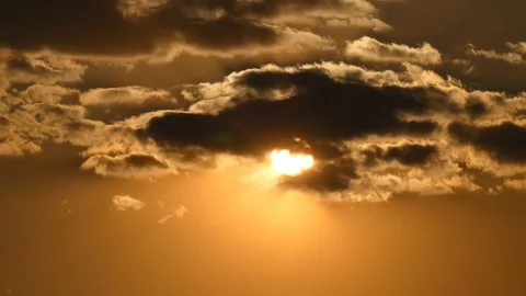 Sun passes through dramatic gray clouds on a golden sky during sunset Stock Footage 248149448