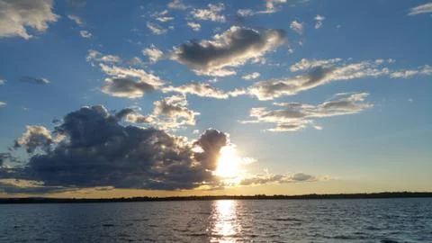 Sun peeking through clouds above lake Foto stock