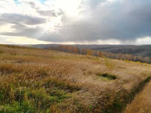 Sun peeking through the clouds over the autumn field Stock Photos