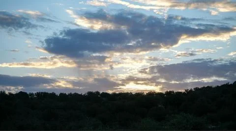 Sun peeking through dramatic clouds over a forest Stock Photos