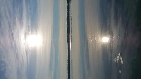 Sun peeking through hovering clouds reflecting on lake Foto stock