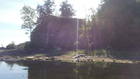 Sun peeking through the trees on a rock ledge on a peninsula on the lake Foto stock
