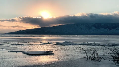 Sun peeks through clouds during dramatic sunset at frozen Utah Lake Stock Footage 242824841