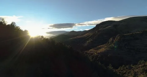 Sun peeks through tree tops down mountain side at sunset drone aerial 4k Stock Footage 125756668