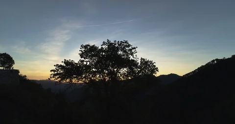 Sun peeps over mountain at dawn from behind tree drone aerial 4k Stock Footage 125754207