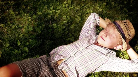 Sun pierces through the tree leaves and wakes up the boy sleeping on the grass 스톡 동영상 74202472