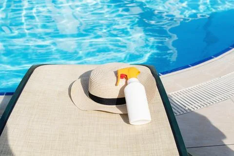 Sun protection essentials on poolside lounger with straw hat beside blue wate Fotos Stock