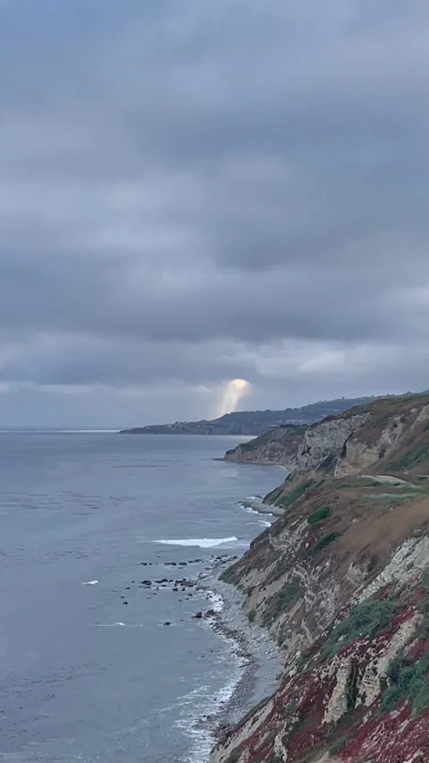 Sun Ray Shines Through Rain Clouds Over Pacific Ocean Cliffside on Rocky Beach Stock Footage 244458918
