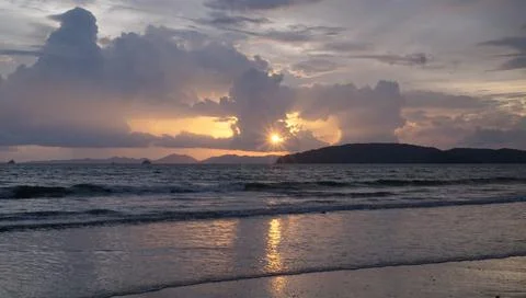Sun rays beaming through clouds reflection onto the waves at a beach during s Stock Photos