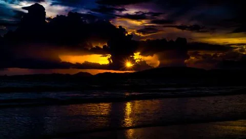 Sun rays beaming through a scatter  of clouds during evening sunset at a beac Stock Photos