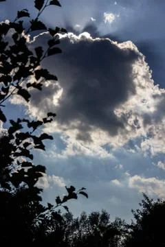 Sun rays behind a dark cloud on a blue sky Stock Photos