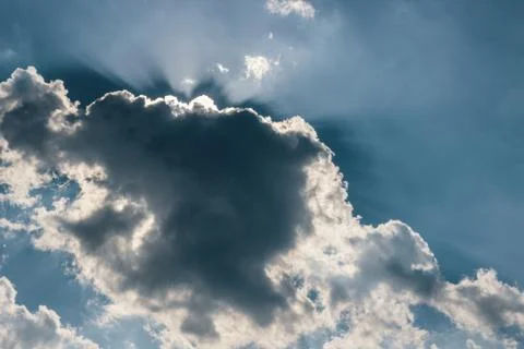 Sun rays behind a dark cloud on a blue sky Stock Photos