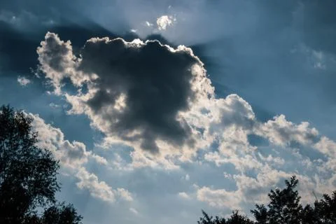 Sun rays behind a dark cloud on a cloudy sky Stock Photos