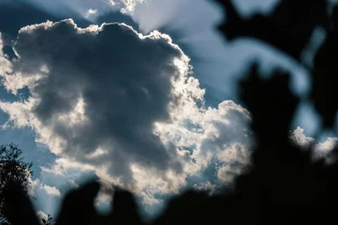 Sun rays behind a dark cloud on a blue sky Stock Photos
