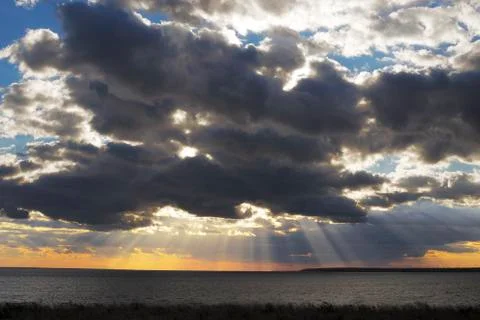 Sun rays behind dark clouds in sky before sunset Stock Photos