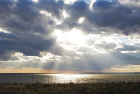 Sun rays behind dark clouds in sky before sunset Stock Photos