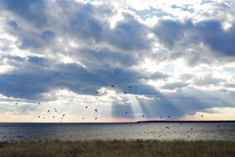 Sun rays behind dark clouds in sky before sunset Stock Photos