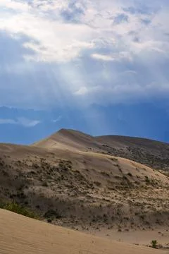 Sun rays breaking through clouds over desert dunes Stock Photos