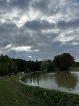 Sun Rays Breaking Through Clouds Over Park Pond. Stock Photos