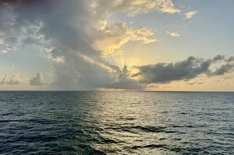 Sun Rays Breaking Through Clouds Over Calm Ocean at Sunrise Stock Photos