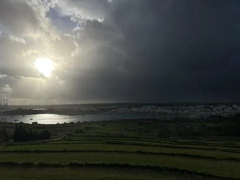 Sun rays breaking through dark storm clouds over green fields Stock Photos