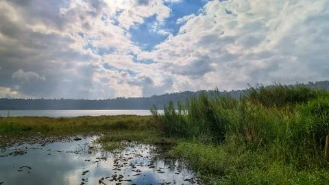 Sun Rays Breaking Through Dramatic Clouds Over Scenic Lake and Reeds Stock Photos