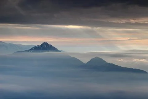 Sun rays burst through dark clouds over peaks in autumn mist Stock Photos