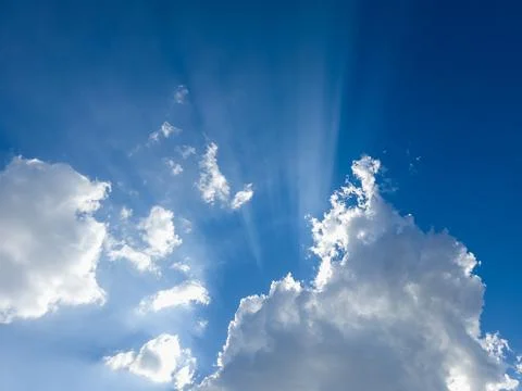 Sun rays burst through dramatic cumulus clouds in vivid blue sky Stock Photos