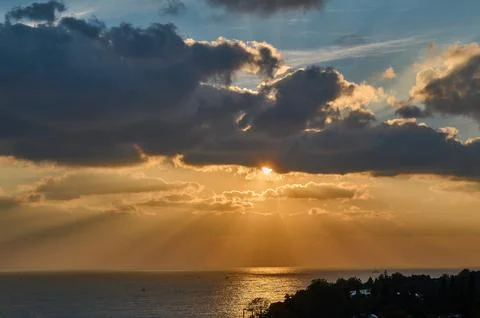 Sun rays from clouds at sunset over the sea Stock Photos