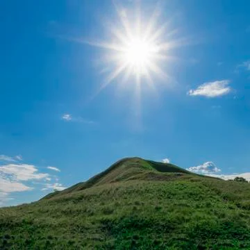 The sun with rays dying in different directions, over a green hill Stock Photos