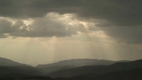 Sun rays emerging through the dark storm clouds passing over the mountain. Stock Footage 230651306