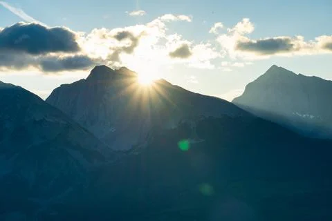 Sun rays illuminate mountain peaks with clouds creating a scenic vista. Stock Photos
