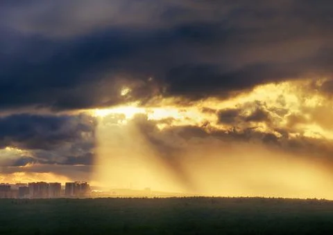 The sun rays make their way through the dark clouds over the forest and city  Foto stock