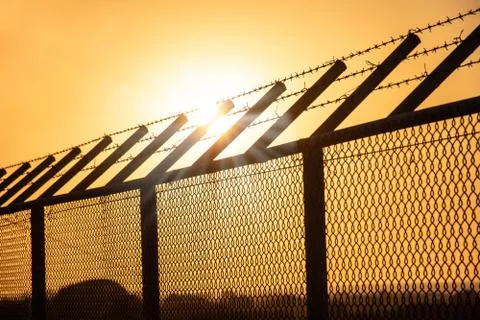 Sun rays over barb wire on metal fence, Sunset Stock Photos