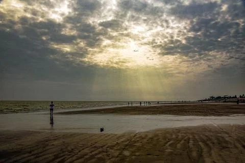 Sun Rays Over Quiet Beach With People By Shoreline and Distant Pier Stock Photos
