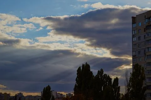 Sun rays pass through the clouds against the sky and houses Stock Photos