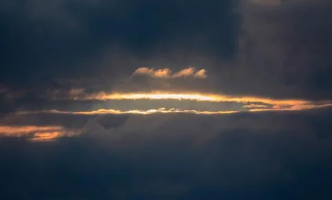 Sun rays passing through clouds in stormy weather during sunset Stock Photos