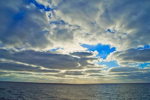 Sun rays passing through dark clouds. The unpredictable drama of the sky. Stock Photos