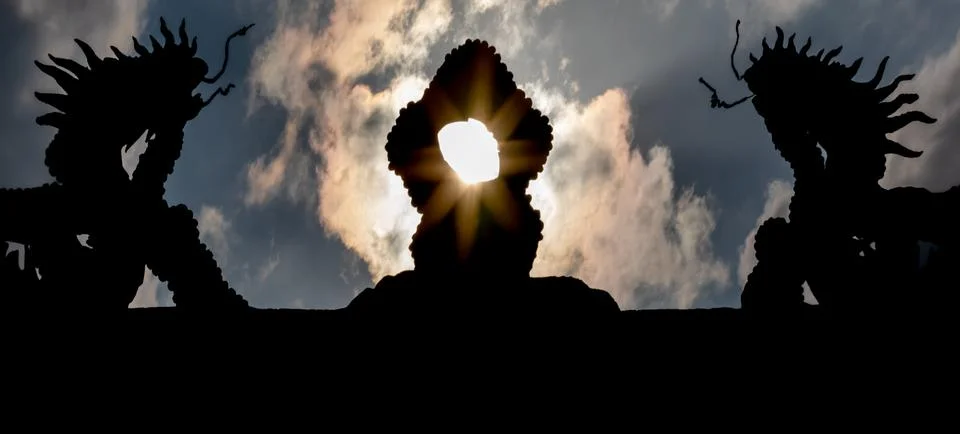 Sun rays passing through silhouette of dragons on temple roof Stock Photos