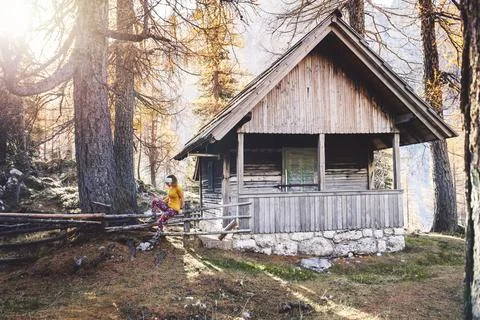 Sun rays peaking trough the forest while woman hikers sits on the fence by a Stock Photos