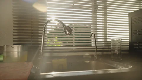 Sun Rays Peeking Through the Gaps of Closed Window Blinds Above a Kitchen Sink Stock Footage 308453583